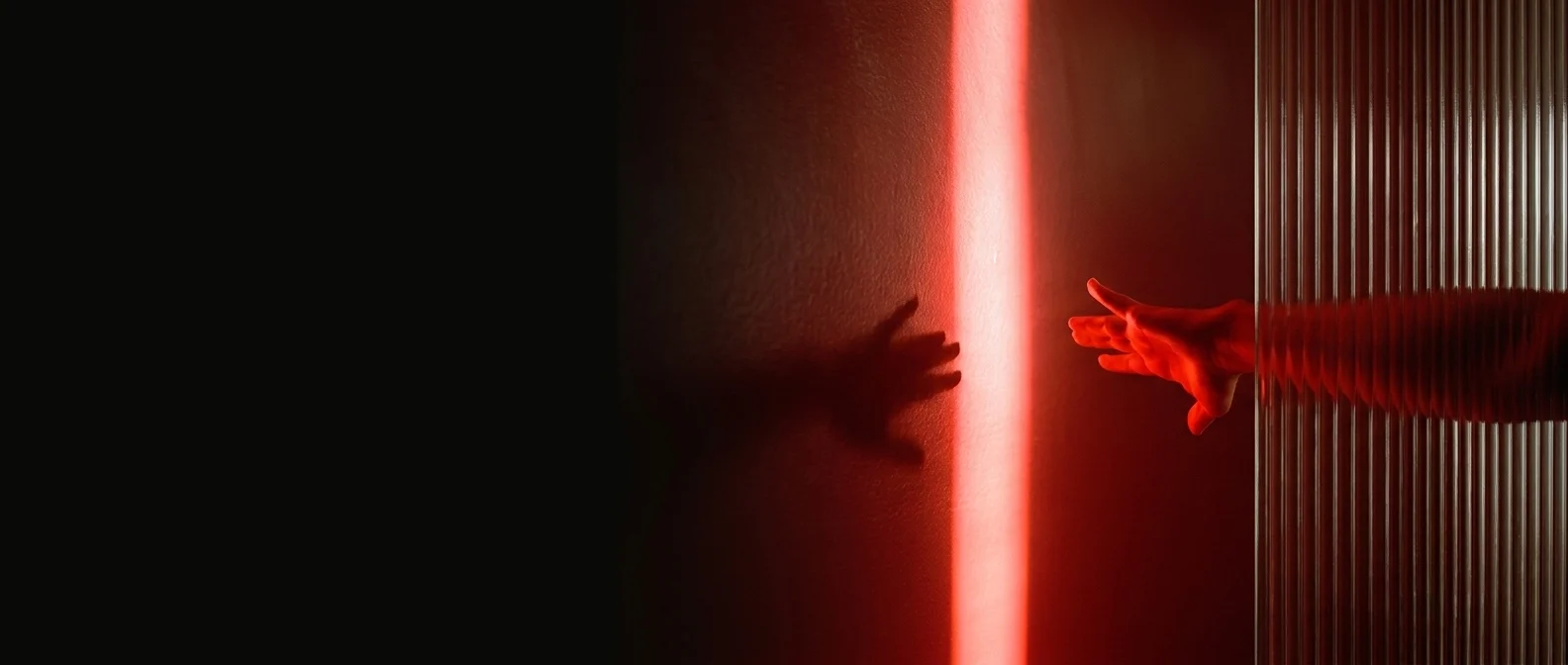 A hand reaching through fluted glass toward a vertical beam of red light